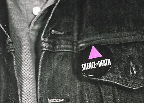 [button with pink triangle on black and white denim jacket reads “SILENCE = DEATH”]